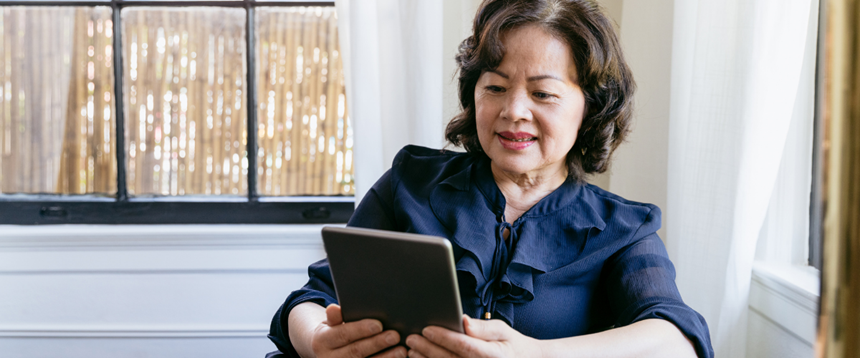 Woman sitting in front of windows reading on a tablet.