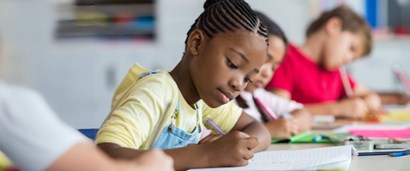 Three children sitting at a table writing in notebooks